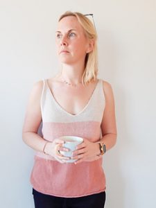 A woman in front of a white wall wears a v-neck sleeveless top in three shades of pink