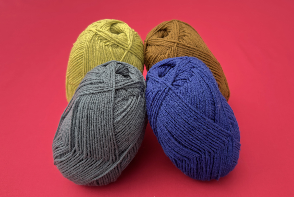 Four skeins of wool yarn in acid yellow, warm rust, electric blue and soft green on a bright red background.