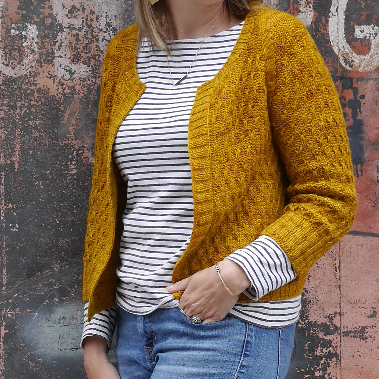 A white woman with light blonde hair models a honeycomb-textured cardigan knitted in deep gold yarn.