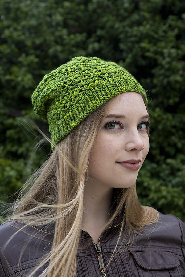 A white woman with long blonde hair wears a slouchy beanie crocheted in bright green yarn.
