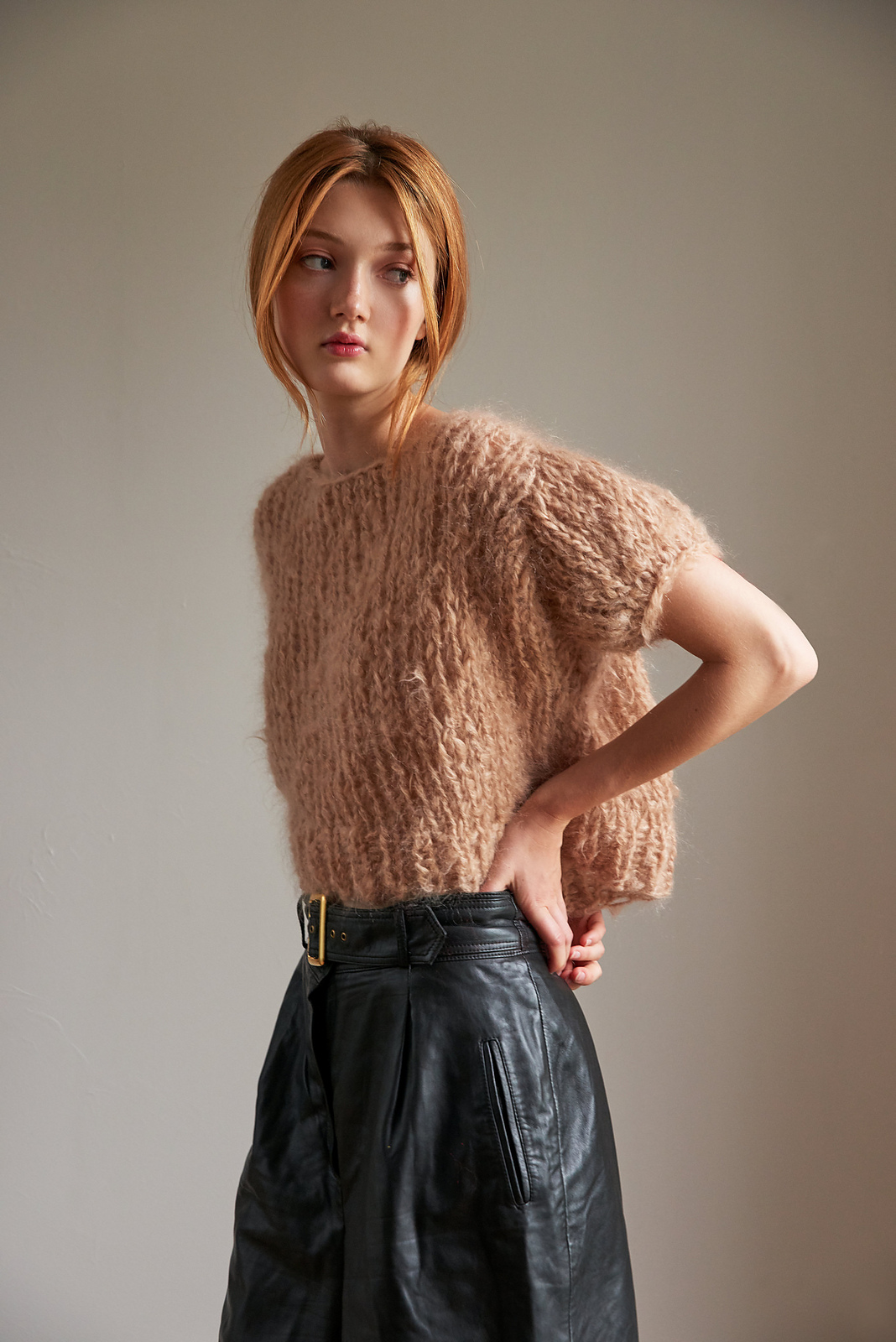 A young white woman with long red hair models a fluffy pullover with short puff sleeves knit in warm beige mohair yarn.