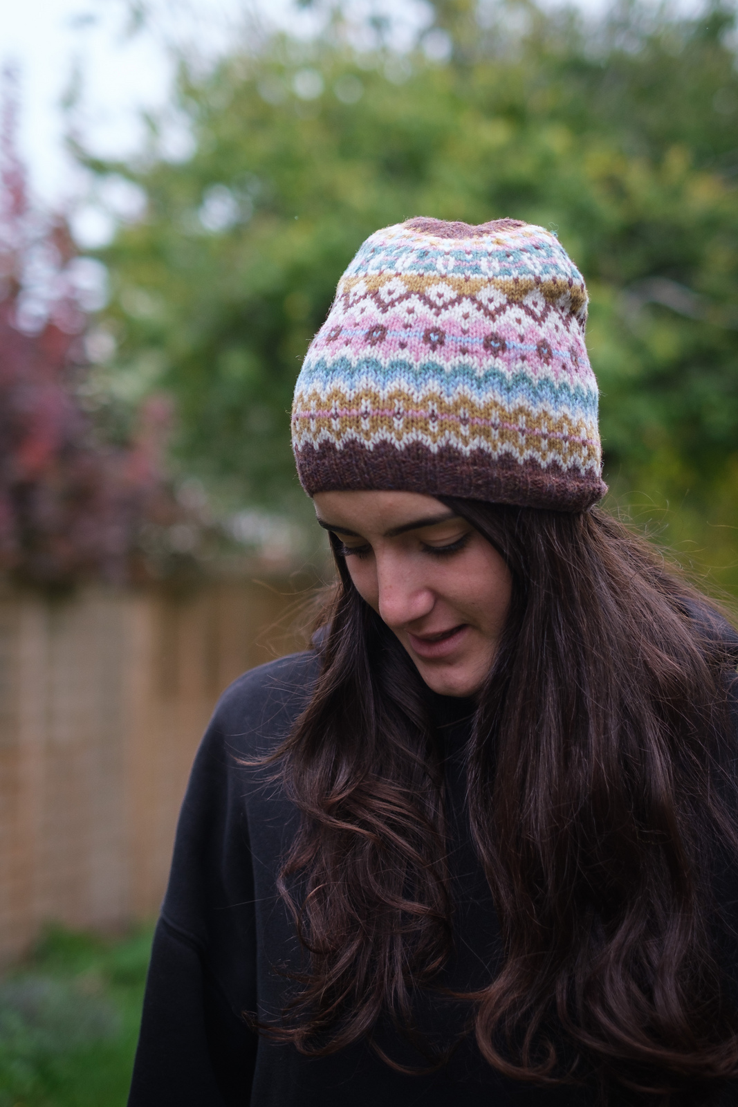 A white woman with long brown hair models a hand knitted colorwork hat.