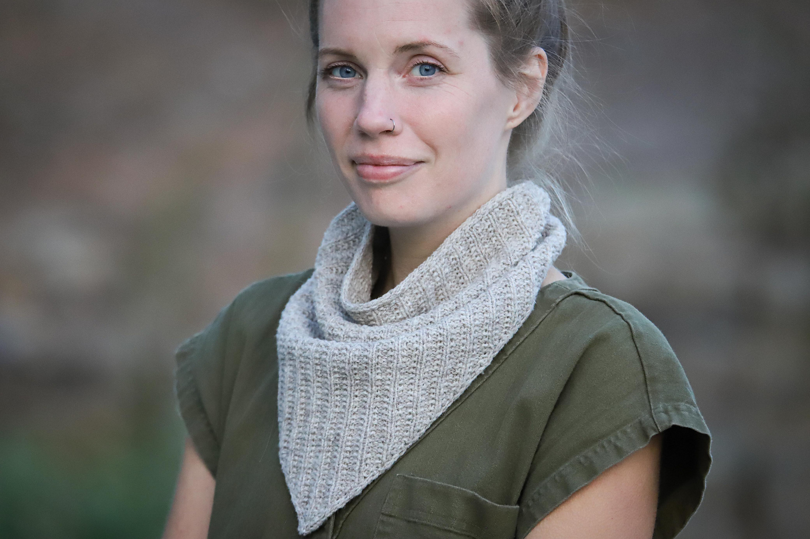 Alicia Plummer, a white woman with dark blonde hair, models a knitted kerchief in pale gray wool yarn.