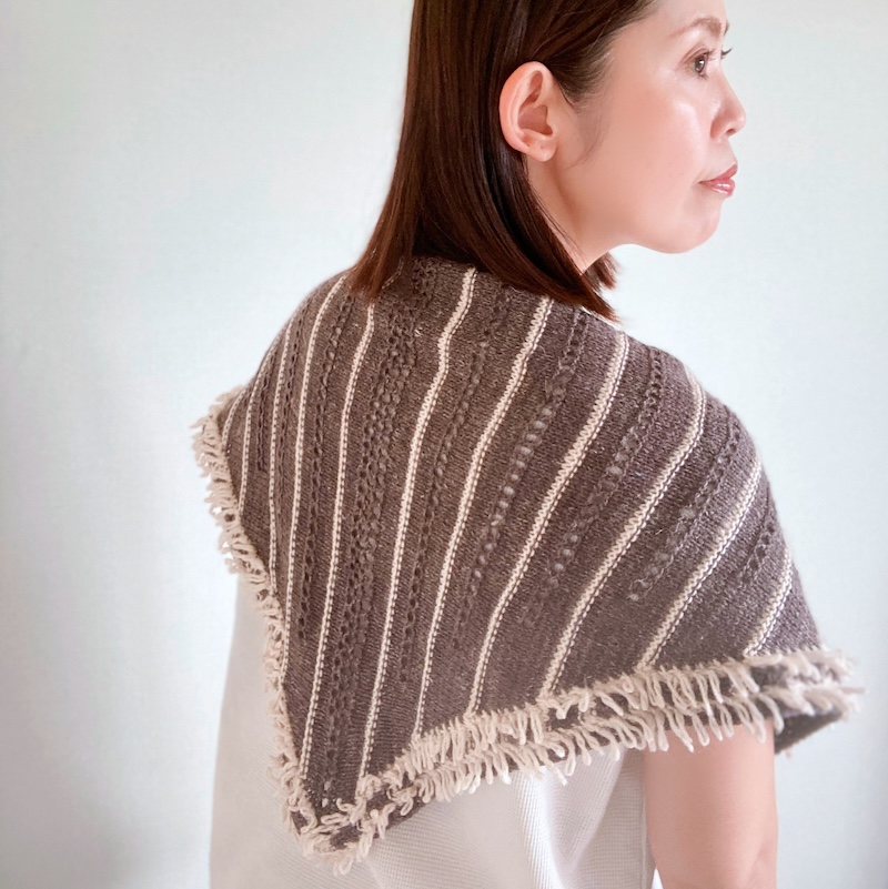 An Asian woman with shoulder-length dark hair models a striped triangular shawl in soft brown and beige.