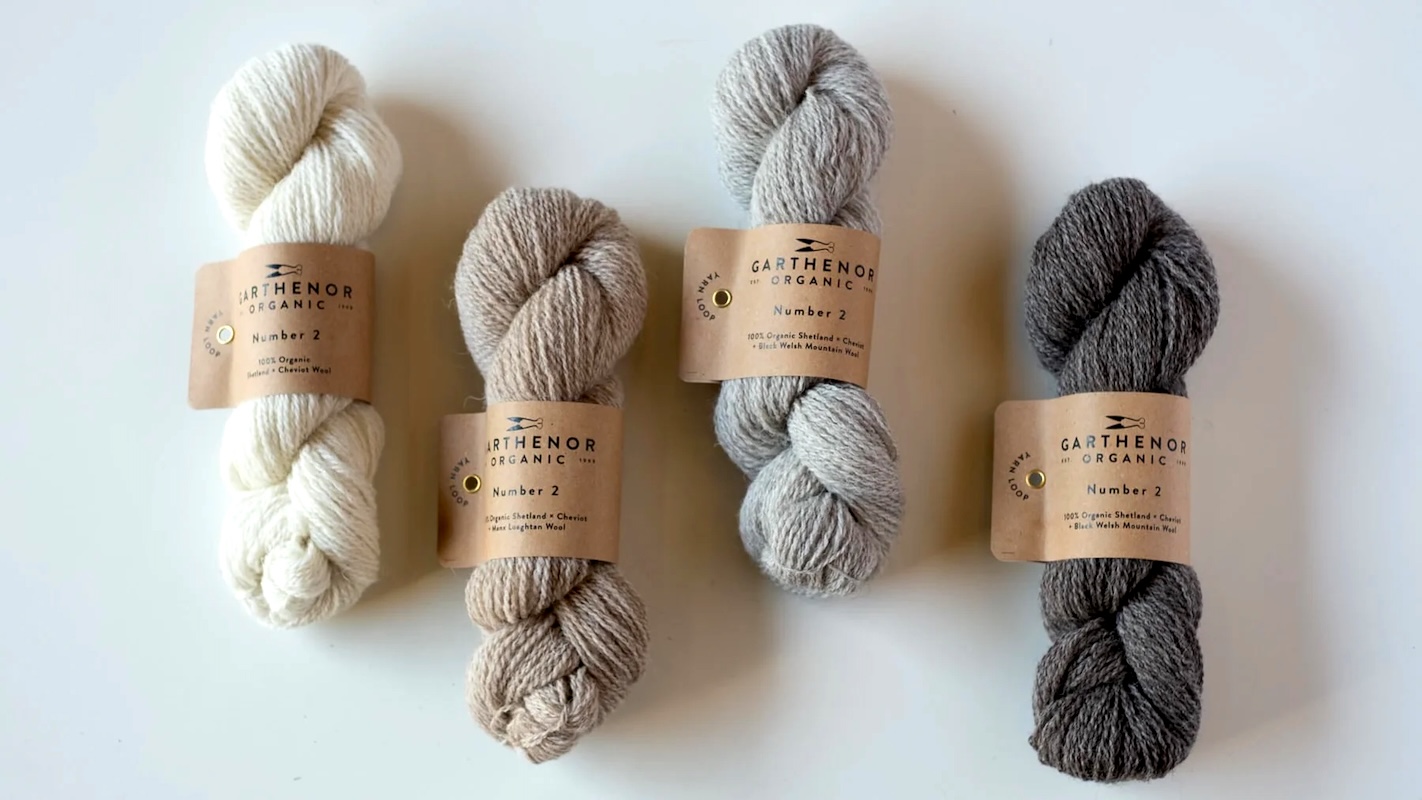 Four skeins of wool yarn in natural white, tan, and gray shades.