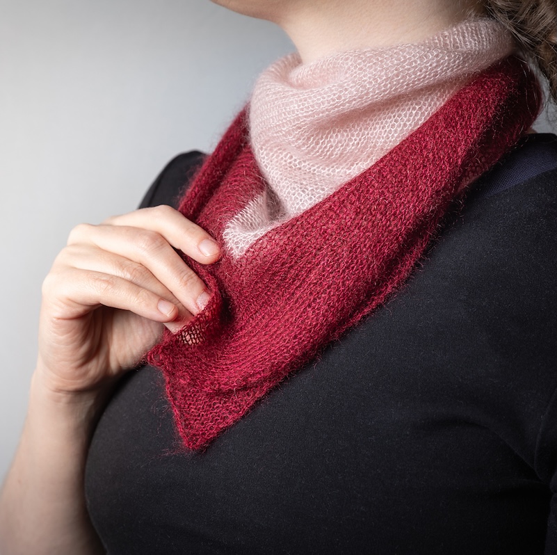 Closeup of a light-skinned person with brown hair wearing a knitted kerchief in fluffy pink and red yarn.
