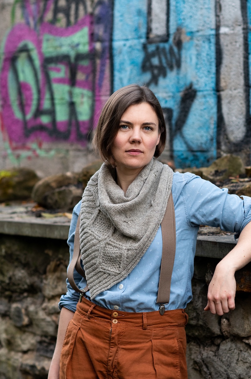 Designer Ysolda Teague, a white woman with short brown hair, models a gray hand knitted shawl