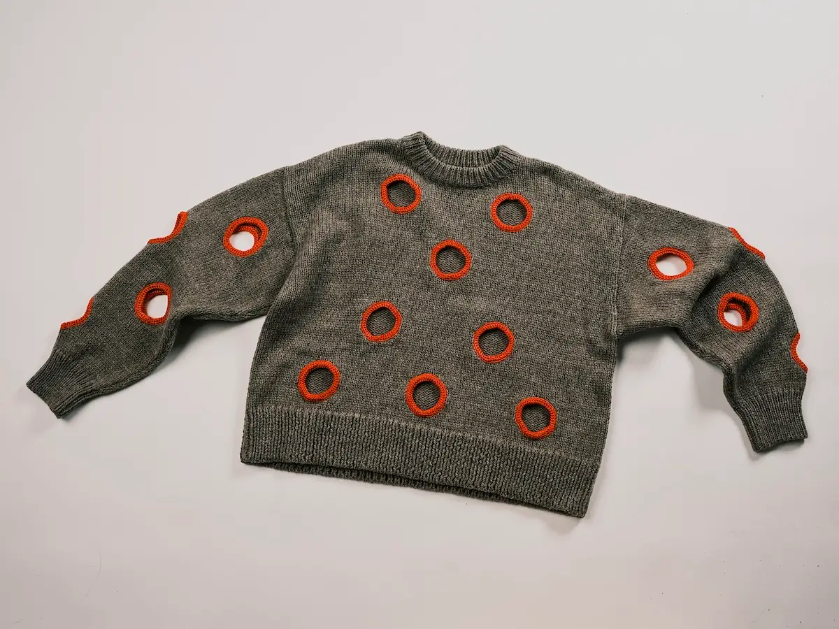 A dark gray-brown knitted sweater decorated with circular cutouts edged in red-orange.