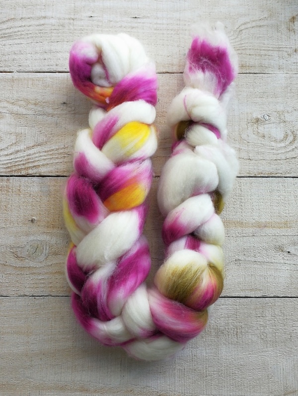 A braid of wool fiber dyed with bright pink and yellow shades.