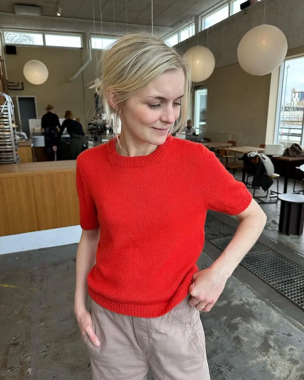 A light-skinned woman with blonde hair models a short-sleeved knitted sweater in bright red.