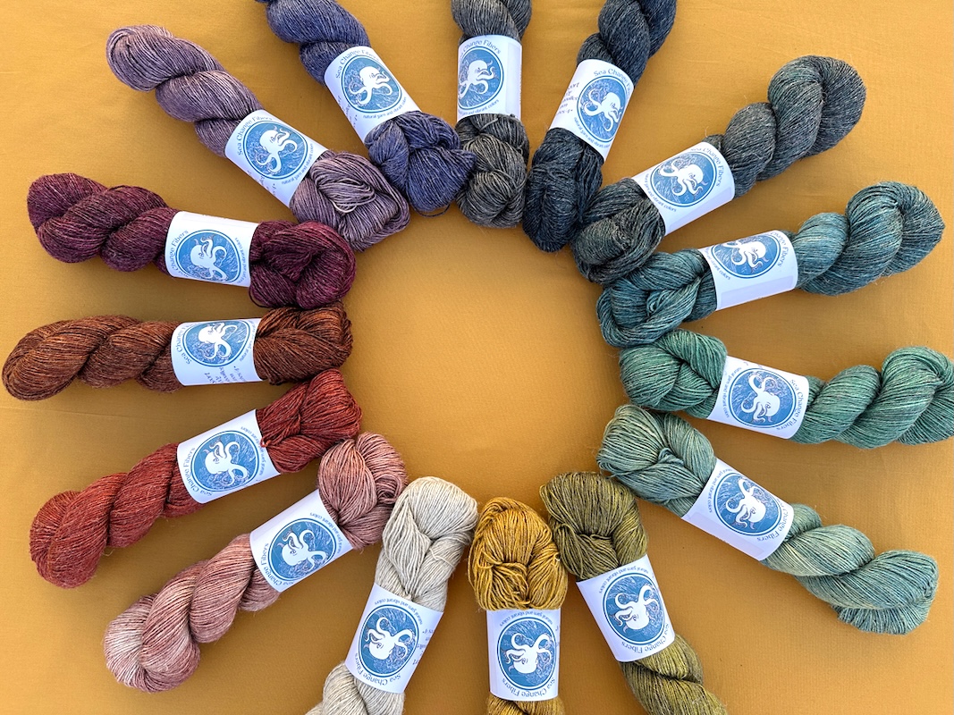 A circle of yarn skeins arranged in color order from reds to purples to blues, greens, and yellows, all on a deep yellow background.