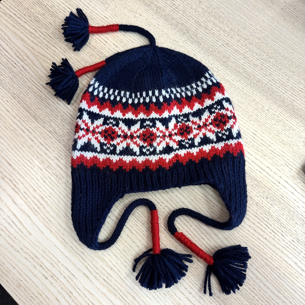 A colorwork hat in navy blue, red, and white with earflaps and tassels.