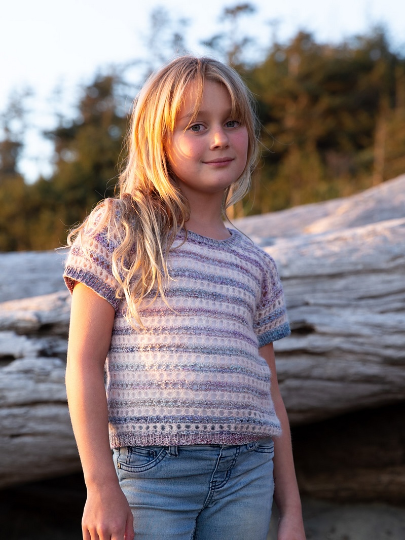 A child with long blonde hair wears a lacy striped short-sleeved sweater.