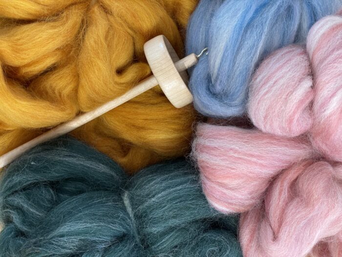 Colorful wool fiber in hues of yellow, blue, green, and pink is arranged around a wooden drop spindle.