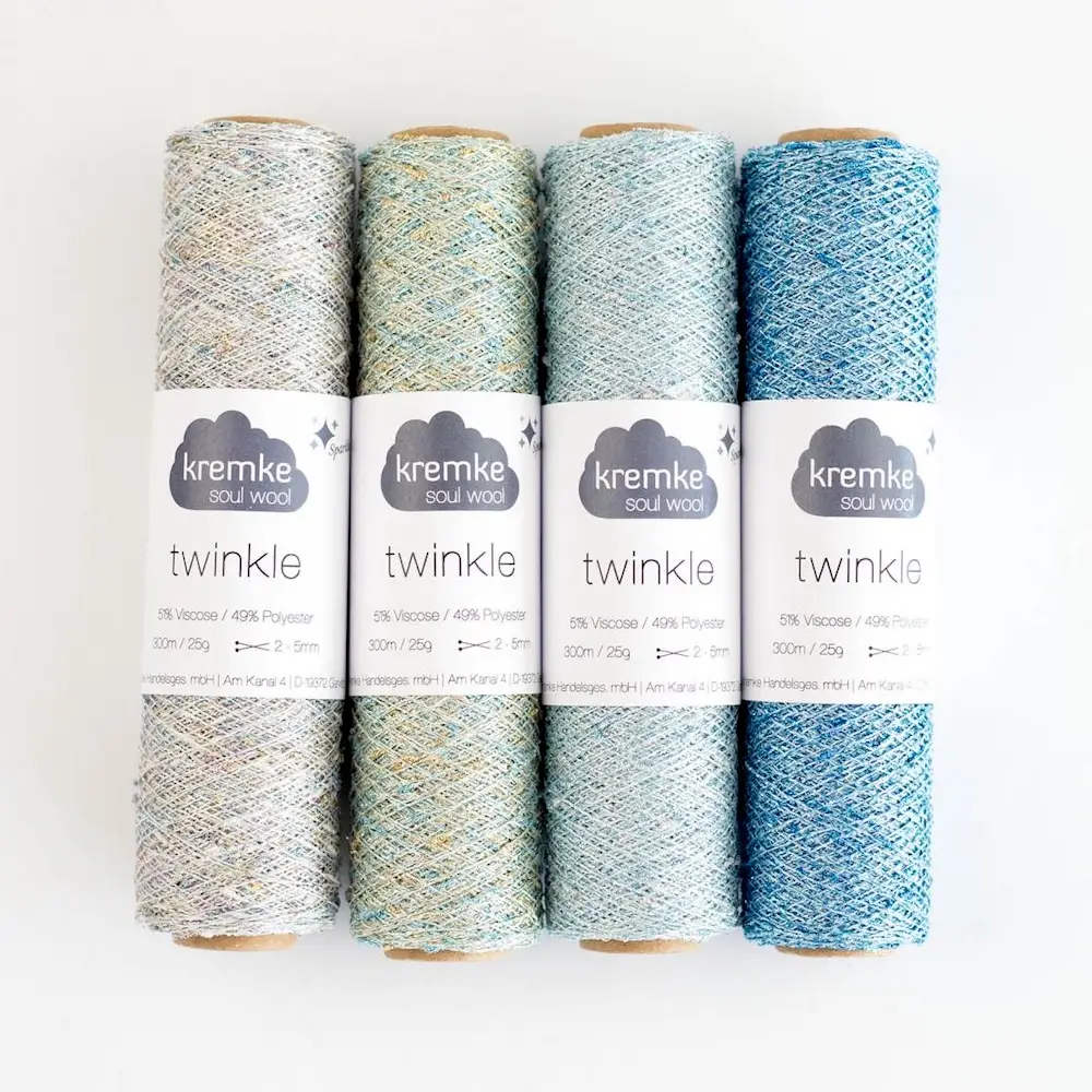 Four spools of Kremke Soul Wool "Twinkle" yarn in metallic shades of silver, pale green, and pale blue.