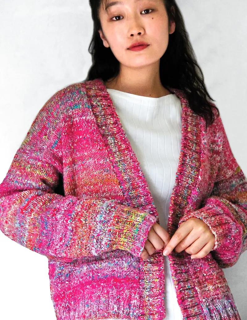 An Asian woman with long dark hair models a chunky knitted cardigan in variegated shades of pink.