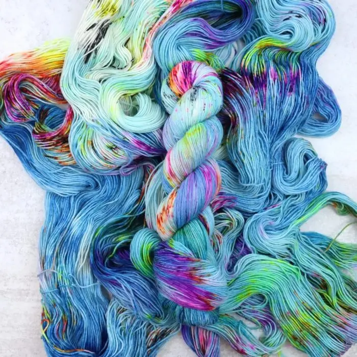 Hand-dyed 4-ply fingering weight yarn featuring a vibrant mix of turquoise, lime green, and magenta speckles.