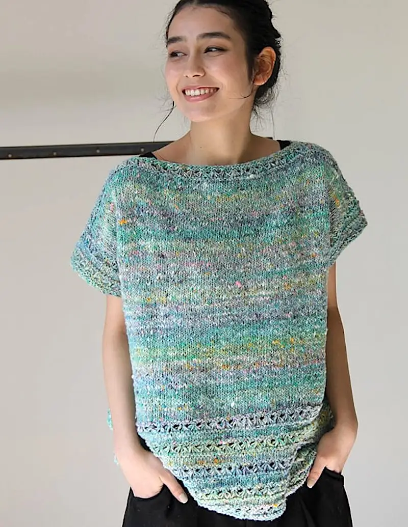 A young Asian woman with dark hair pulled back, smiling and looking off-camera. She is wearing a short-sleeved, boat-neck sweater striped in shades of blue, green, and cream. The sweater has a slightly oversized fit and delicate eyelet details near the hem. 