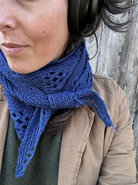 a woman wears a royal blue knit neck scarf with a lace flower design throughout
