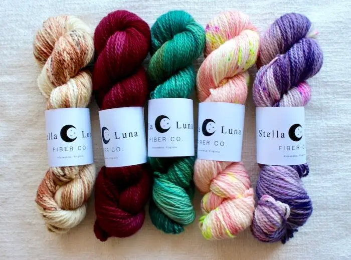 Skeins of hand dyed Stella Luna yarn in variegated and tonal brown, deep red, cool green, bright peach, pink and purple shades.