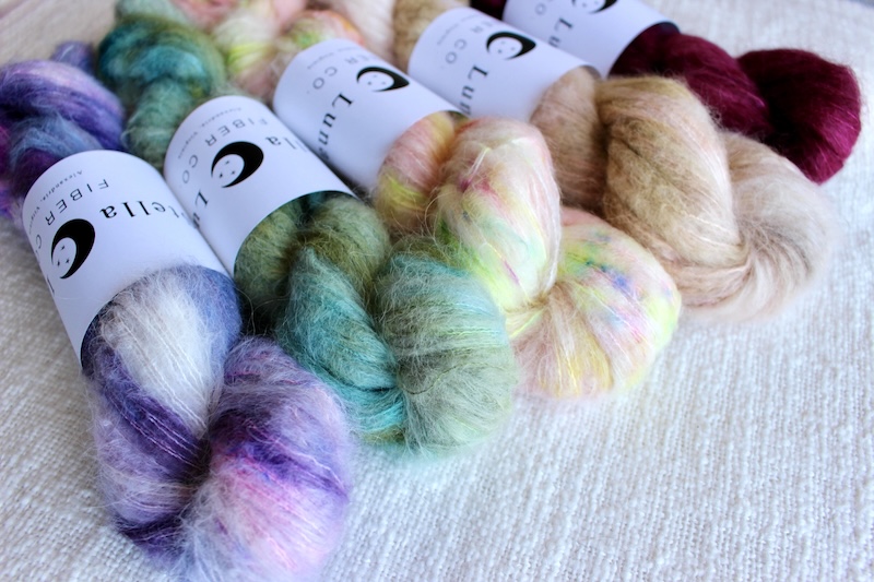 Fluffy hand dyed skeins of alpaca and silk yarn in bright purple, green, peach, and magenta shades.