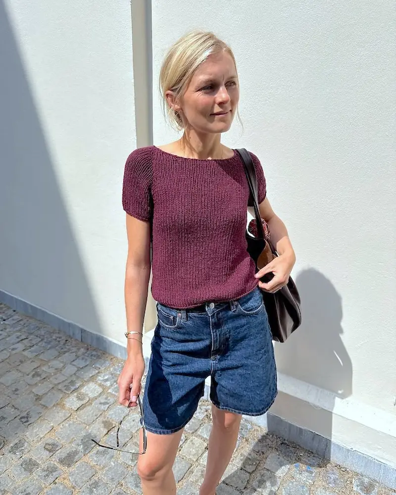 A blonde person wearing a chunky knitted tee in burgundy.