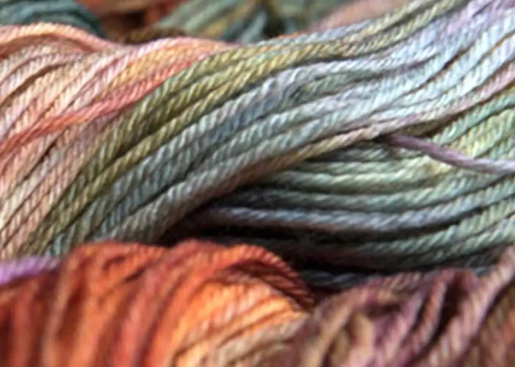 Closeup of skeins of hand-dyed Malabrigo yarn in soft greens, blues, and orange shades.