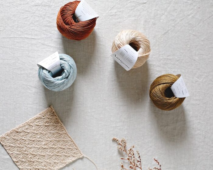 Four balls of De Rerum Natura Antigone linen yarn in pale blue, rust, beige and olive.