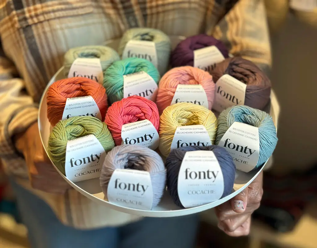 Person holding a white tray filled with colorful Fonty brand yarn balls in various pastel and vibrant shades.
