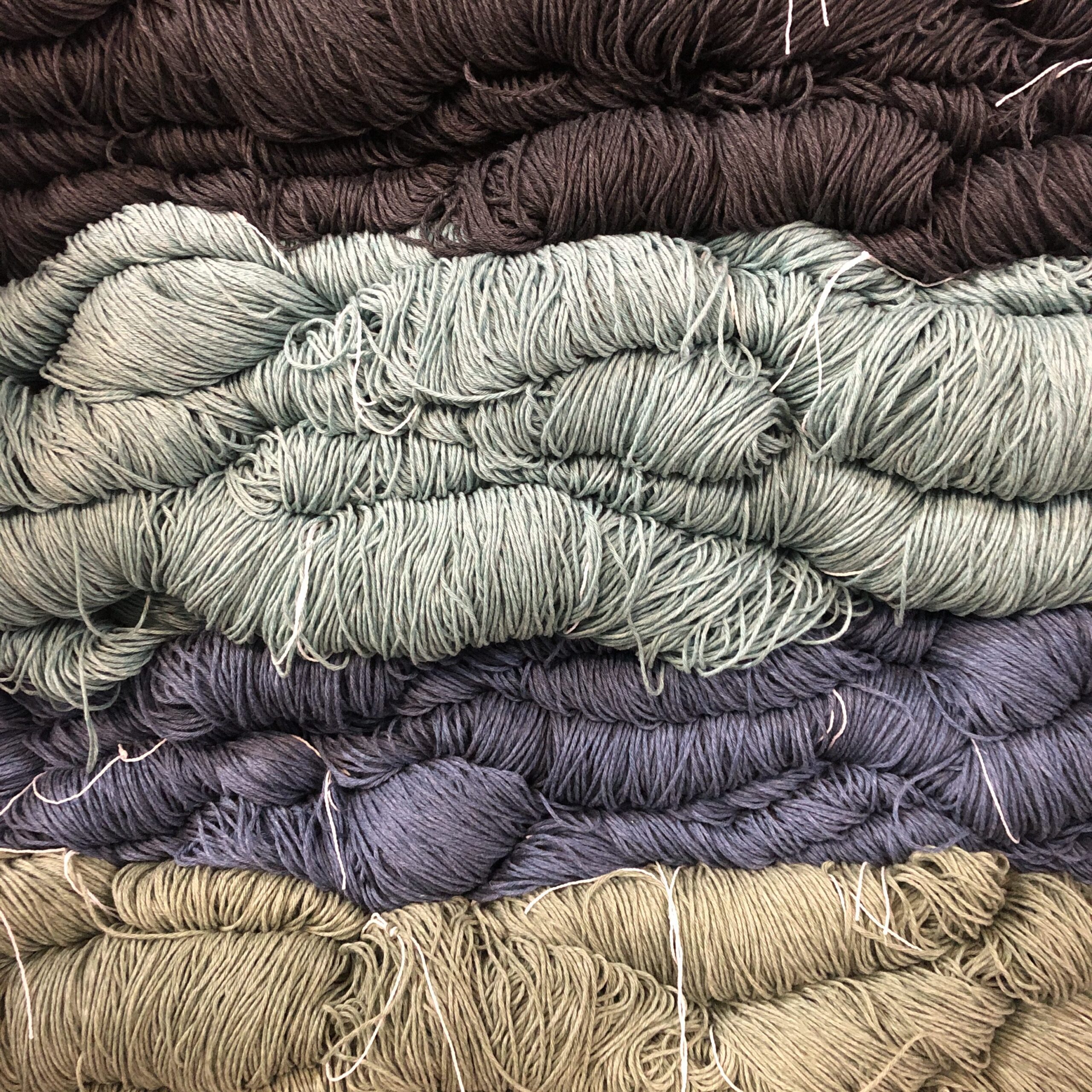 Stacks of loosely wound yarn in the Fonty factory in dark brown, light gray, navy blue, and olive green colors.
