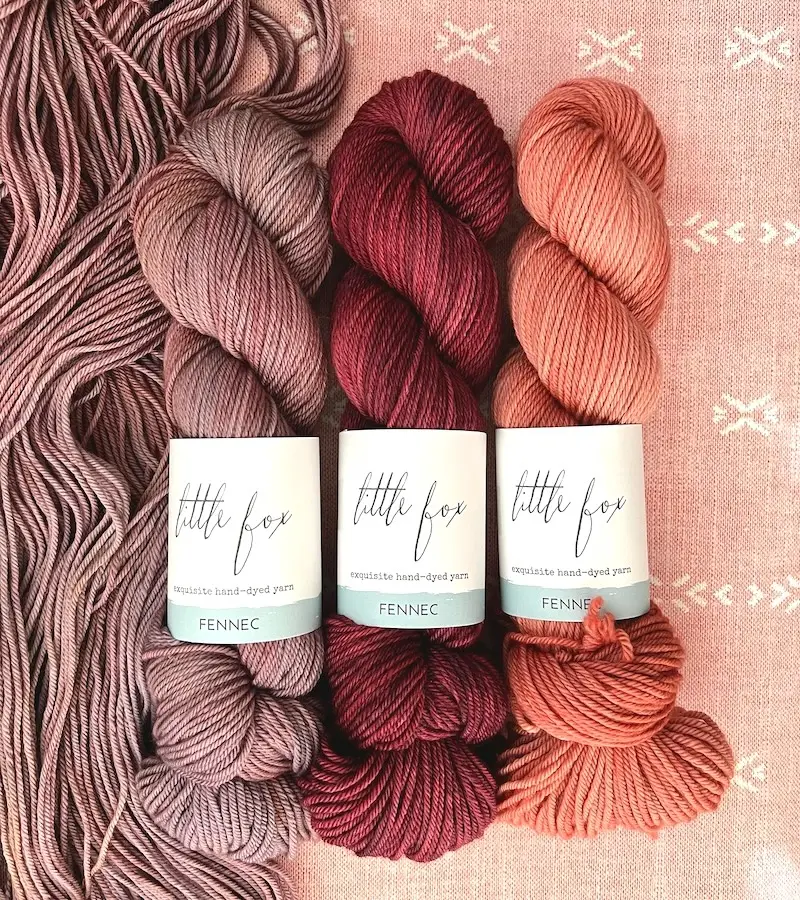 Three skeins of Little Fox Fennec yarn in mauve, deep red, and rich peach.