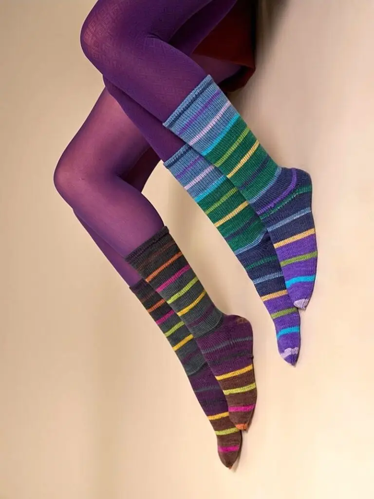 Closeup of two people in purple tights wearing striped socks knitted in Laines du Nord Indulgence Sock yarn.