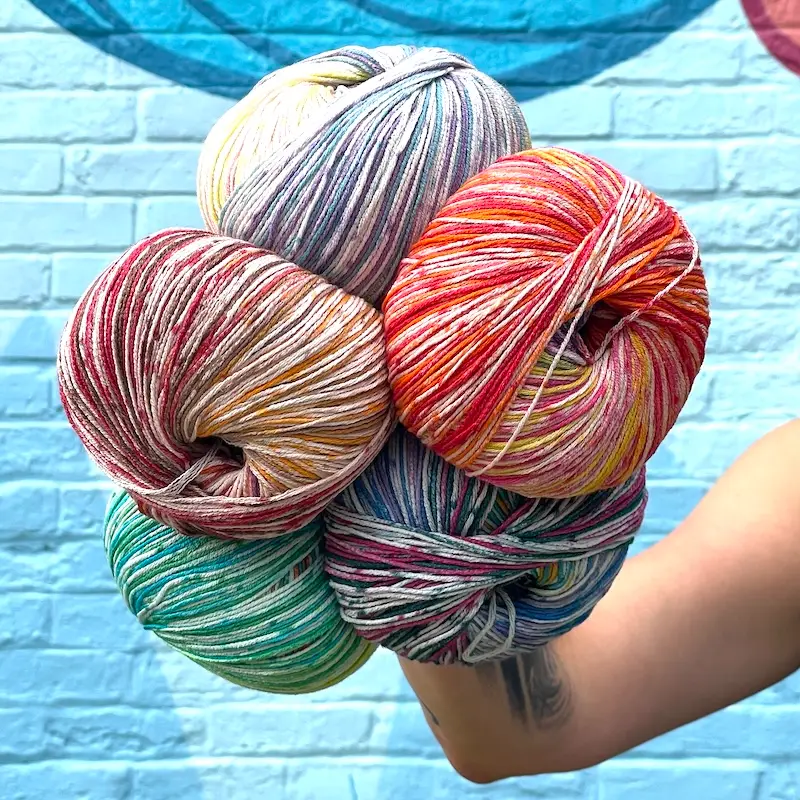 Closeup of a person holding five giant balls of colorful speckly yarn in one hand