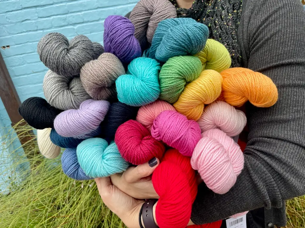 A person in a gray sweater holds a rainbow of colors of hanks of Blue Sky Fibre yarn.