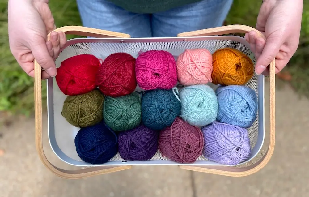 A person's hands hold a basket of Rosarios 4 BioWool skeins in multiple colors