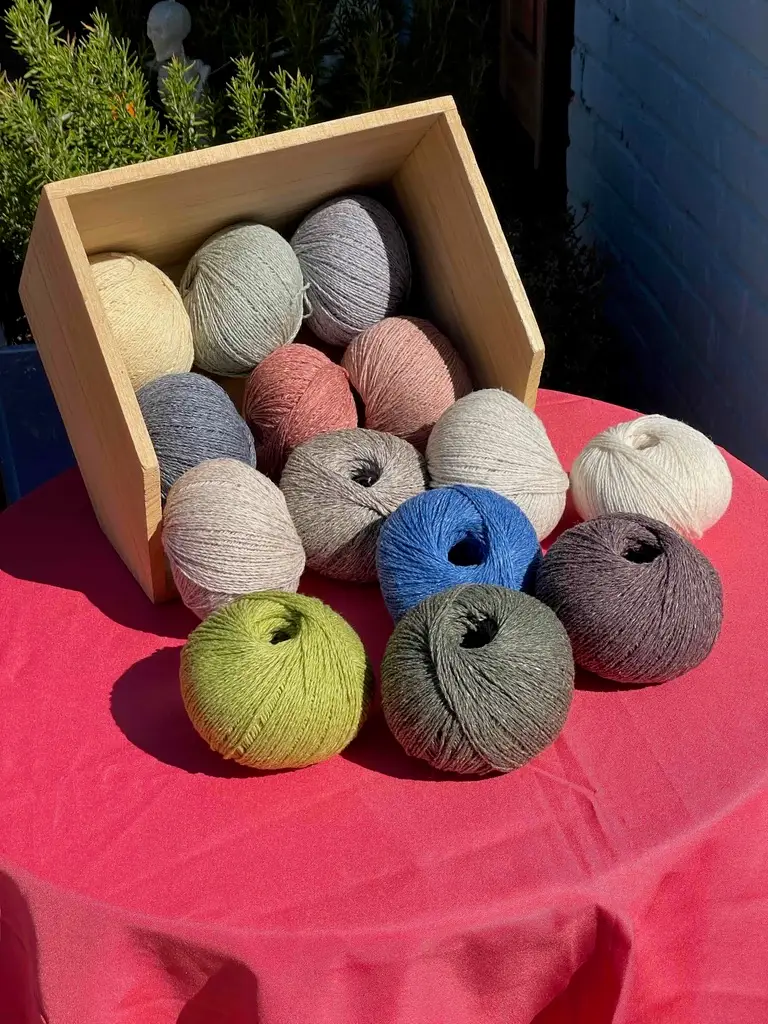 Balls of Wooldreamers Saona spill from a wooden crate onto a table with a raspberry-colored tablecloth