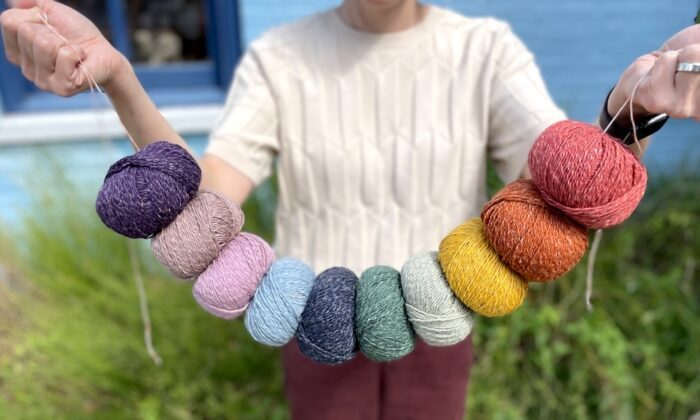 Closeup of a person in a white sweater holding a string of yarn balls arranged in rainbow color order.