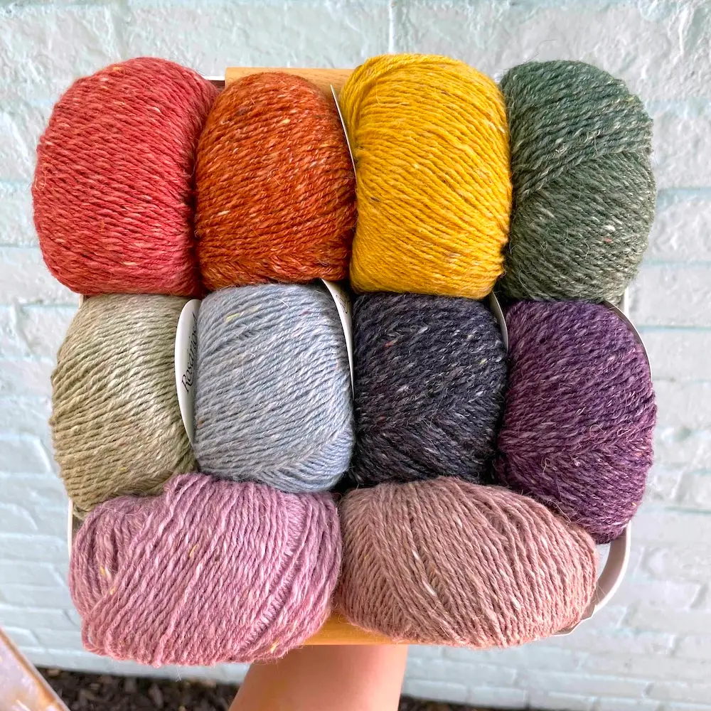 Closeup of a person's hand holding up a basket stuffed with balls of tweedy yarn