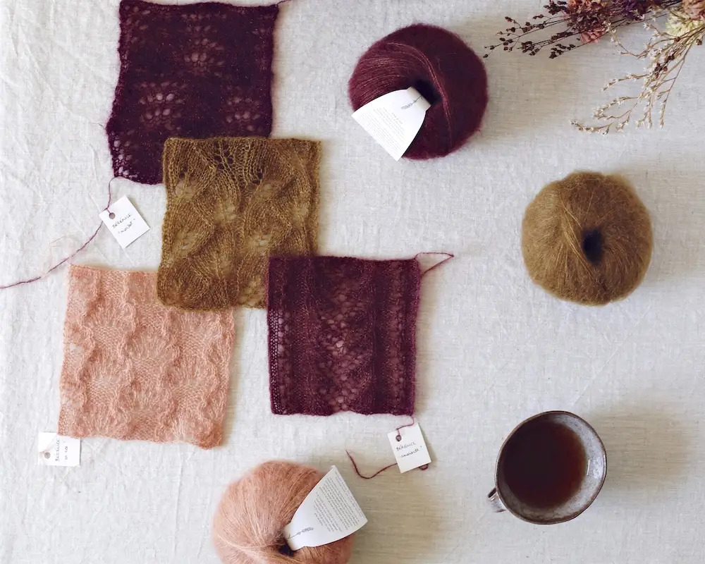 Balls and swatches of fuzzy De Rerum Natura Bérénice yarn on a linen-covered table.