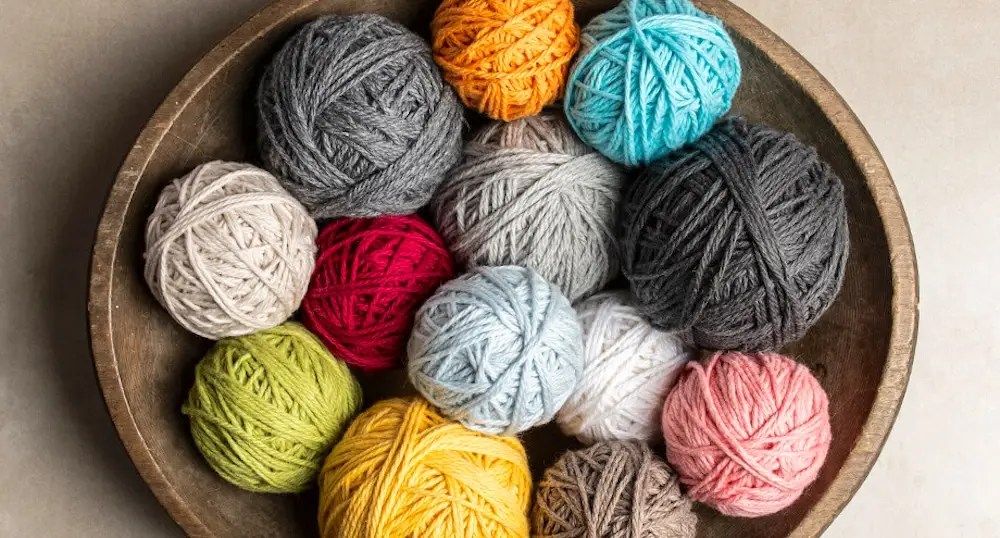 Balls of Blue Sky Fibers Sweater yarn in a wooden bowl.