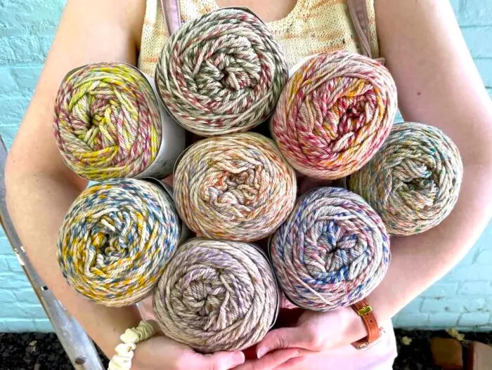 Closeup of a person holding several large skeins of multicolored yarn in their arms