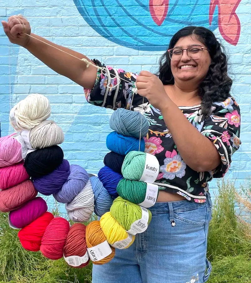 A happy yarnista holds up a string of colorful balls of Fonty Felletin yarn