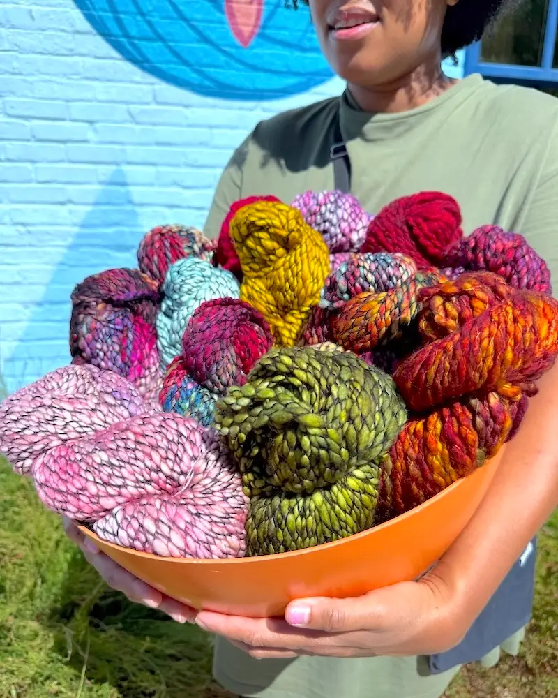 Darian holds a large orange bowl filled with colorful skeins of Malabrigo Caracol 