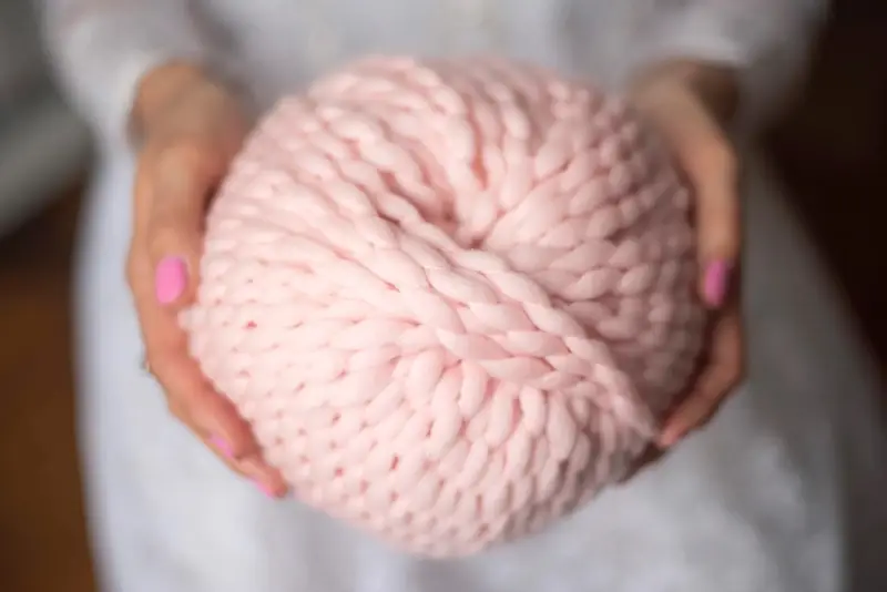 A person's hands hold a giant ball of Loopy Mango Merino No. 5 yarn in soft pink